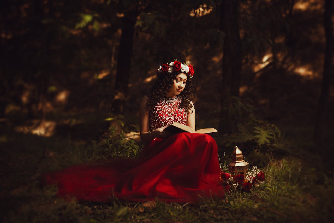 home-hero A woman in a red dress reads a book in a fairytale-like forest setting.